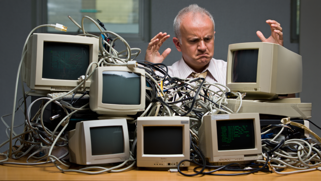 Person looking frustrated by tangled wires and old computers, representing legacy system challenges.